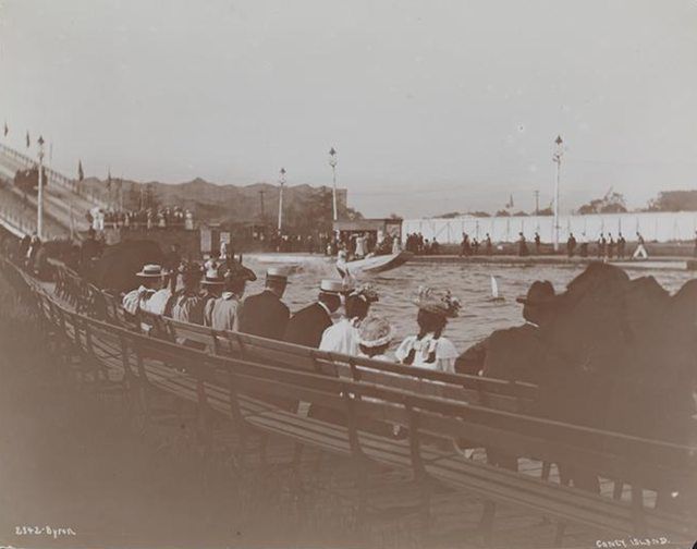 "Spectators watching a boat of an amusement ride after its descent from an inclined chute at Coney Island. 1896."